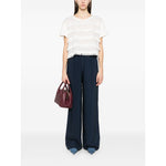 Woman wearing Emporio Armani T-shirt with fringes, white with embroidered logo, paired with blue wide-leg pants, holding a burgundy bag.