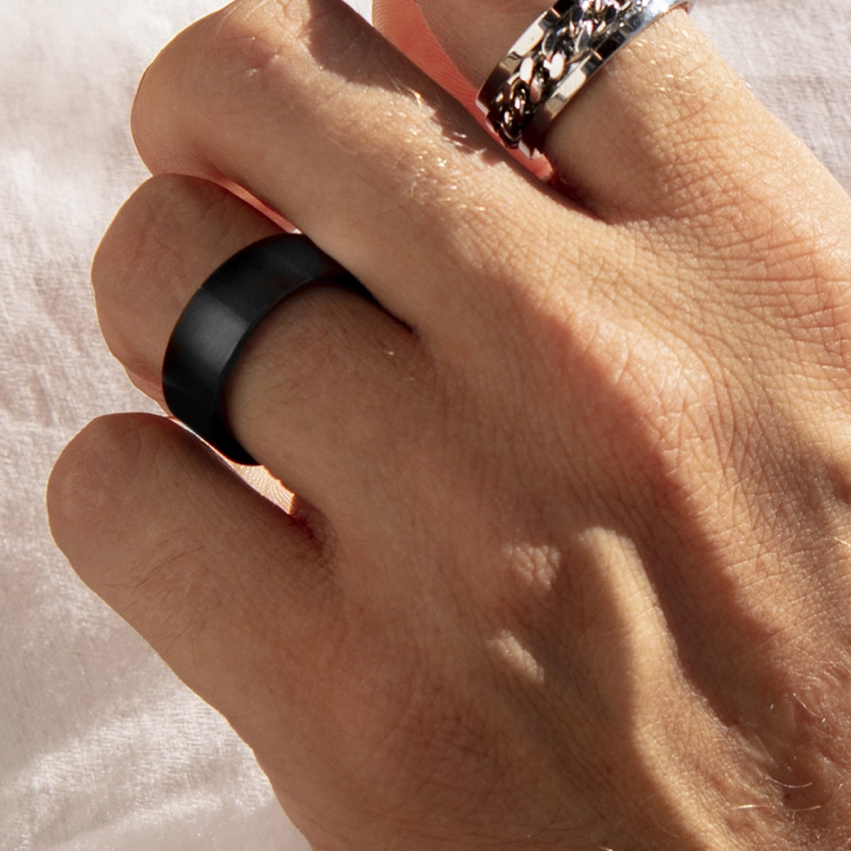 Close-up of a hand wearing a black ring and silver ring against a soft fabric background.