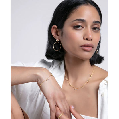 Woman wearing elegant gold jewelry including earrings, necklace, and bracelet, styled with a white shirt, showcasing modern fashion.